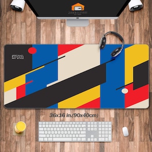 May include: A rectangular mouse pad with a colorful abstract design in the Bauhaus art style. The pad features a geometric pattern with red, blue, yellow, black, and cream-colored shapes. The pad measures 36 x 16 inches.