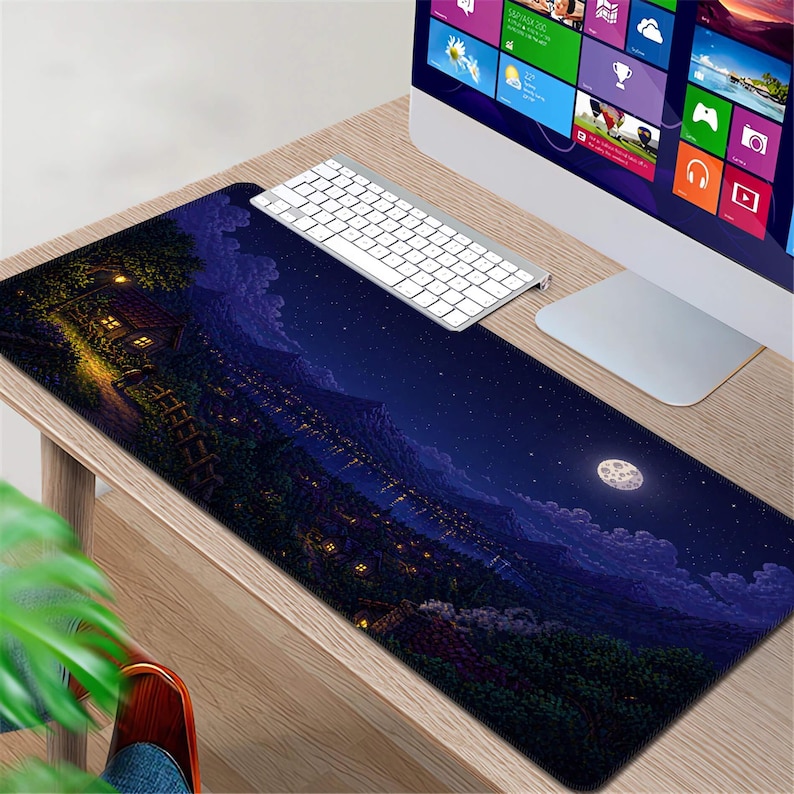 May include: A rectangular mouse pad featuring a nighttime landscape with a full moon, a starry sky, and a village nestled in the valley. A white keyboard and computer monitor are on a wooden desk.