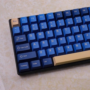 May include: A close-up of a mechanical keyboard with blue keycaps and a beige space bar. The keys are arranged in a standard QWERTY layout. The keyboard has a black frame.