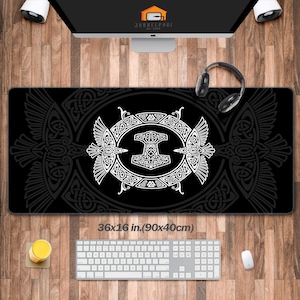 May include: Black rectangular desk mat with a white Viking design featuring a hammer symbol and intricate knotwork. The mat measures 36x16 inches. The design is framed by two stylized birds. The mat is designed for use with a computer.