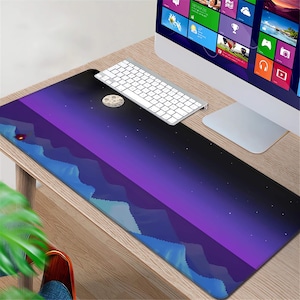 May include: A rectangular mouse pad featuring a stylized night sky design. The pad has a gradient of purple and black, with a crescent moon, stars, and blue mountain silhouettes. A white keyboard rests on the pad.