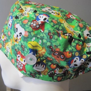 May include: Green scrub hat with a pattern of Animal Crossing characters, including Tom Nook, Isabelle, and K.K. Slider. The hat has a button closure.