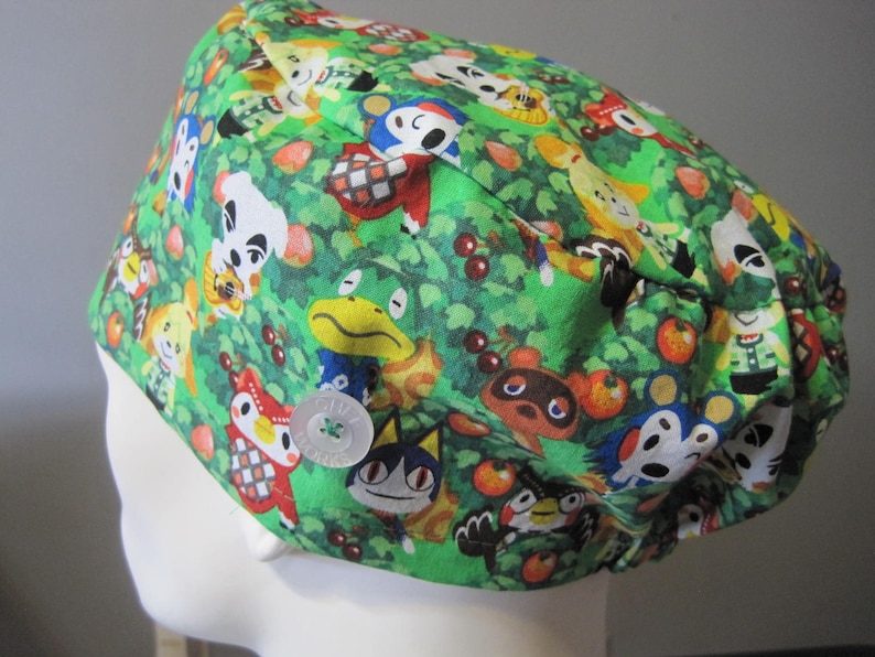 May include: Green scrub hat with a pattern of Animal Crossing characters, including Tom Nook, Isabelle, and K.K. Slider. The hat has a button closure.