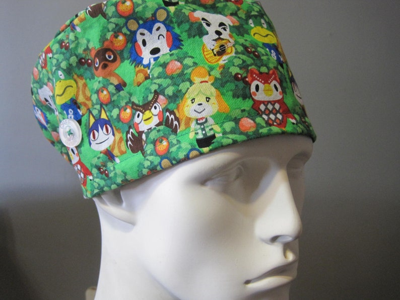 May include: Green scrub hat with a pattern of Animal Crossing characters, including Tom Nook, Isabelle, and K.K. Slider.
