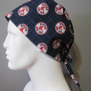 May include: A blue and white surgical scrub hat with a repeating pattern of the Boston Red Sox logo. The hat has a long tie that can be tied at the back of the neck.