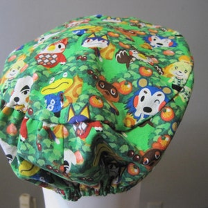 May include: A green fabric hat with a colorful pattern of animal characters from the Animal Crossing video game series. The hat has a gathered elastic band around the bottom.