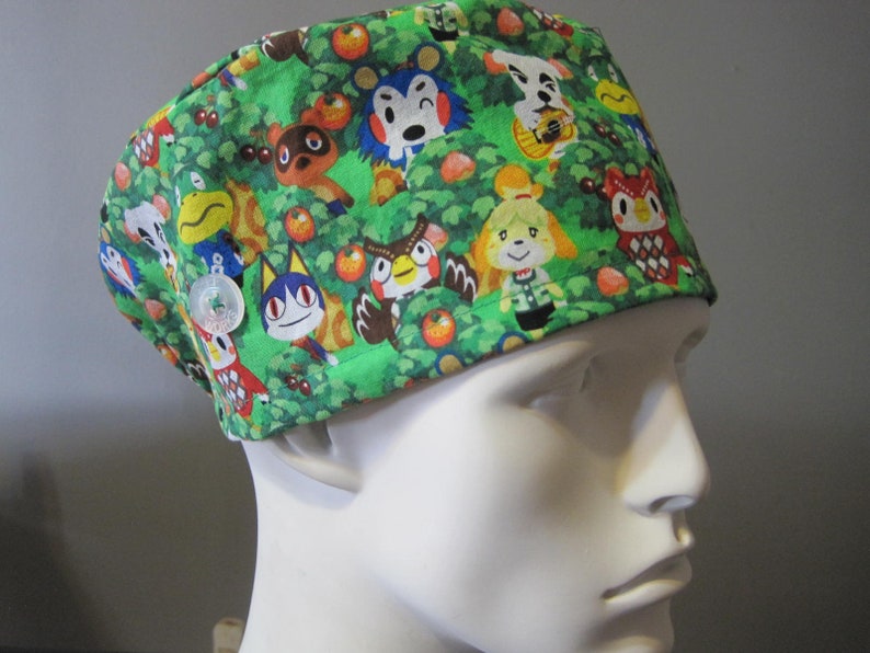 May include: Green scrub hat with a colorful print of various animal characters from the Animal Crossing video game series.
