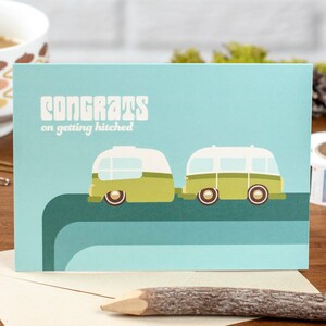 May include: A light blue card with the text "Congrats on getting hitched" and a cartoon illustration of two green and white camper vans driving side by side.
