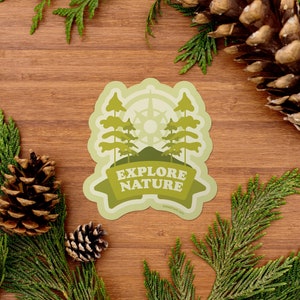 May include: A green and yellow sticker with a compass, trees, and a mountain. The sticker says "Explore Nature" with the website "dailypick.com" below.