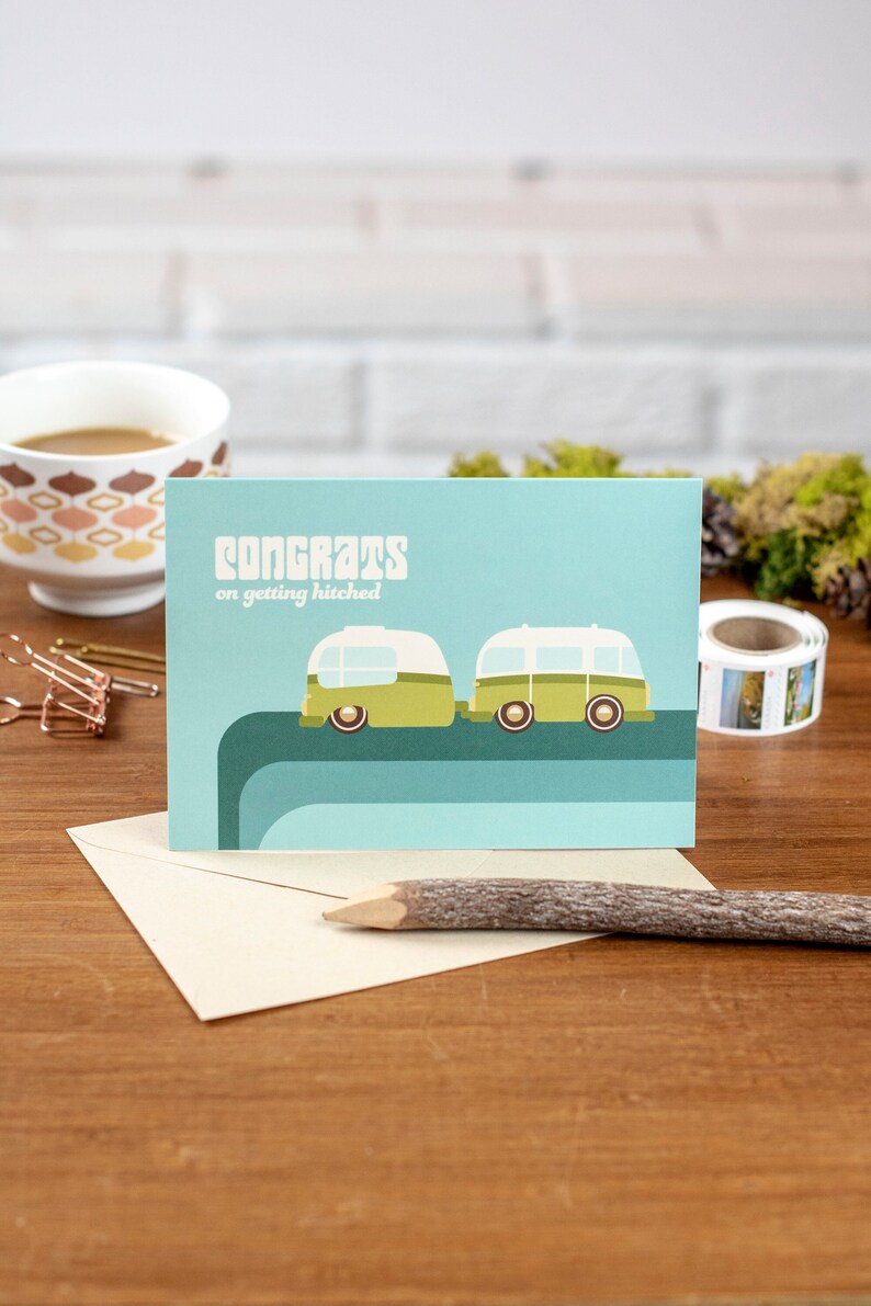 May include: A light blue card with the text "Congrats on getting hitched" and a cartoon illustration of two green and white camper vans driving side by side.