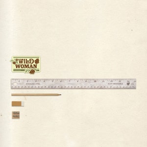 May include: An assortment of stationery items including a pencil, eraser, and pencil sharpener, alongside a 15-inch stainless steel ruler. A sticker with the text "WILD WOMAN" is also present.