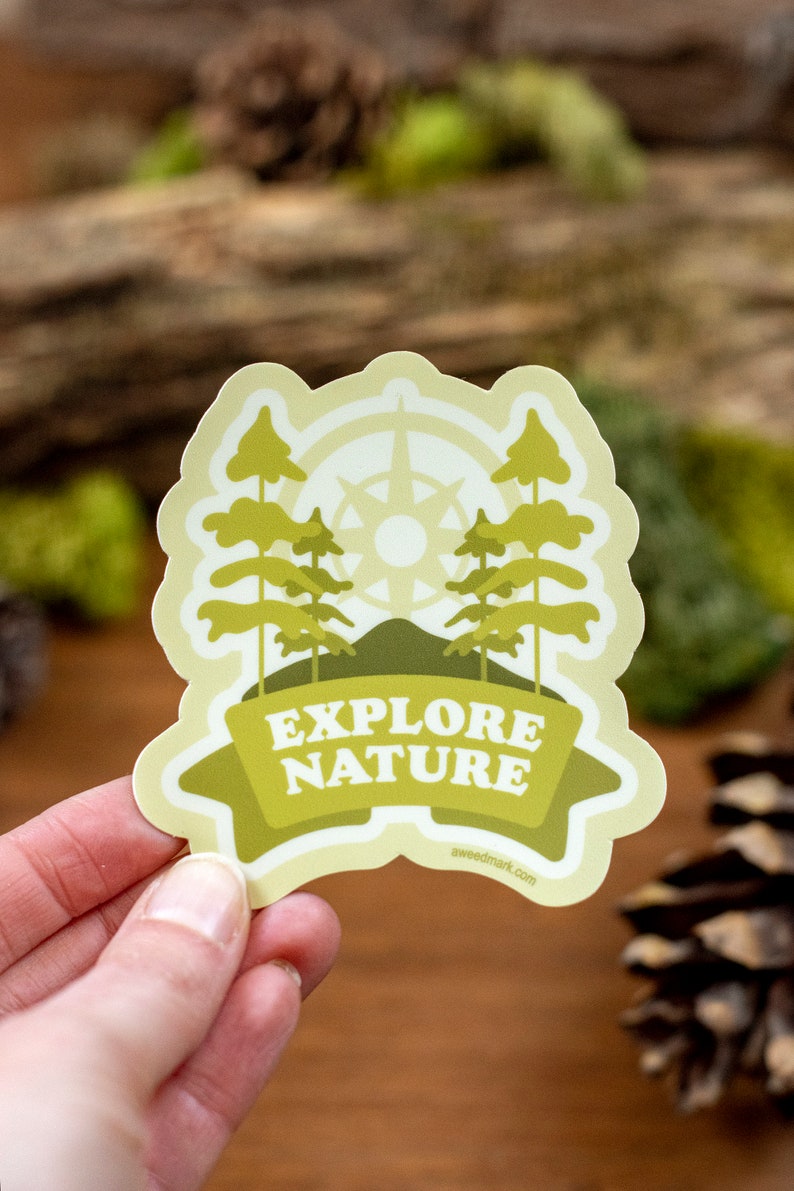 May include: A yellow and green sticker with a compass, trees, and a mountain. The sticker says "Explore Nature" and has the website "aweemark.com" at the bottom.