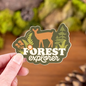 May include: A green sticker with a brown deer, green trees, and ferns. The text "FOREST explorer" is written in white on the sticker.
