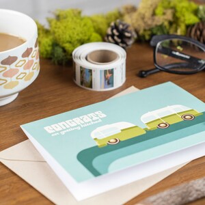 May include: A light blue card with the text "Congrats on getting hitched" and a green and white illustration of two camper vans. The card is sitting on a brown envelope.