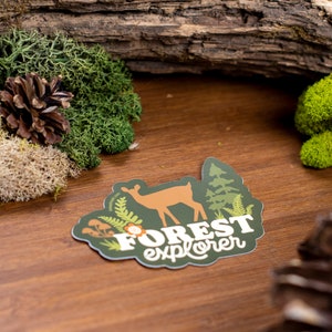 May include: A green and brown sticker with a deer silhouette, forest foliage, and the text "FOREST explorer".
