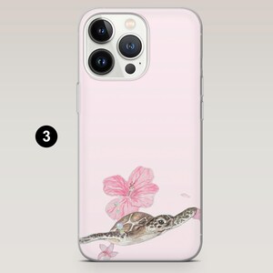 May include: Pink phone case featuring a watercolor illustration of a sea turtle swimming near pink hibiscus flowers. The case has a clear border and a camera cutout. The number "3" is in a black circle in the upper left corner.