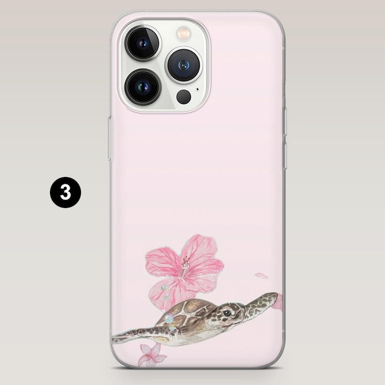 May include: Pink phone case featuring a watercolor illustration of a sea turtle swimming near pink hibiscus flowers. The case has a clear border and a camera cutout. The number "3" is in a black circle in the upper left corner.