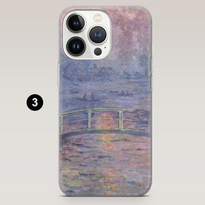 May include: Transparent phone case displaying a Monet-style artwork of a bridge over water, using soft blues, greens, and purples. The painting shows a peaceful landscape with a bridge and water lilies, creating a sense of calm.