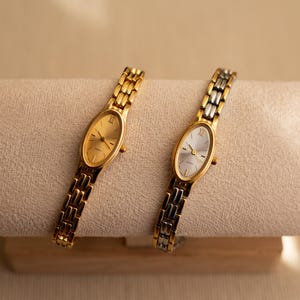 Pode incluir: Dois rel&oacute;gios de quartzo dourados com mostradores ovais e pulseiras de elos. Um rel&oacute;gio tem mostrador dourado, o outro prateado. N&uacute;meros romanos marcam as horas. Os rel&oacute;gios s&atilde;o exibidos em uma superf&iacute;cie bege.