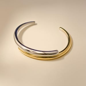 May include: A silver and gold bangle bracelet with a simple, modern design.