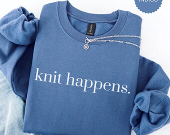 May include: A blue sweatshirt with the text "knit happens." in white lettering. The sweatshirt is folded and displayed on a white background.