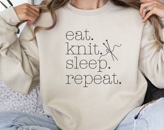 May include: A beige sweatshirt with the text "eat. knit. sleep. repeat." and a graphic of knitting needles and yarn.