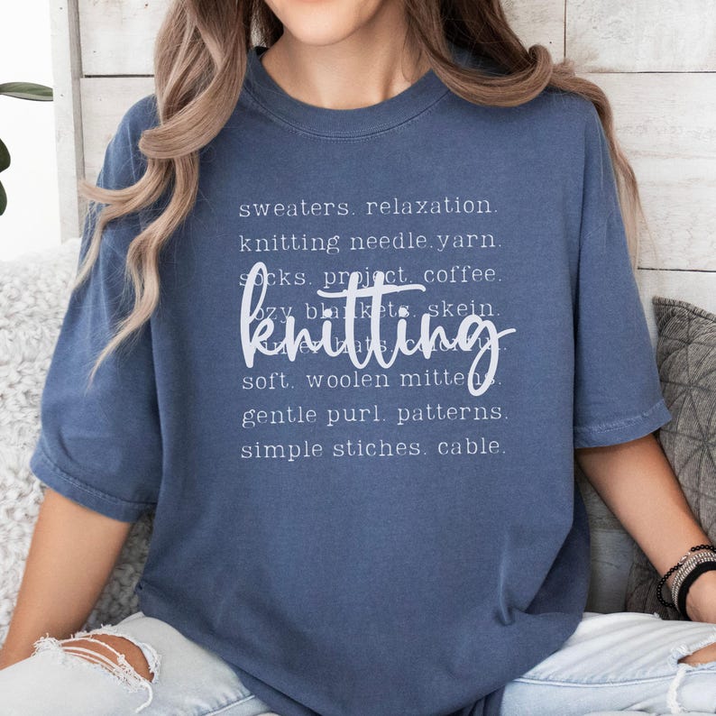 May include: A blue t-shirt with the word "knitting" in a cursive font. The shirt has a list of knitting-related words in a smaller font, including "sweaters," "yarn," and "patterns."