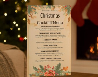May include: A Christmas cocktail menu on a table, held by a gold-colored stand. The menu features festive drink names like "Winter Wonder Spritz" and "Gingerbread Eggnog", with decorative floral accents.