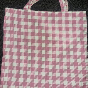 May include: A pink and white gingham tote bag with a floral print on the inside of the handles.