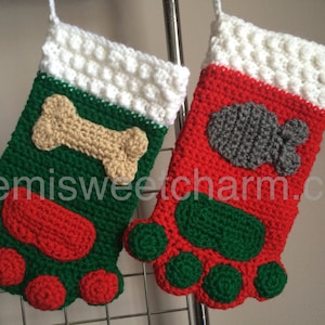 May include: Two crocheted Christmas stockings with paw print bottoms. One stocking is red with a gray fish applique and the other is green with a tan bone applique.  Semisweetcharm.com is printed on the bottom of the stockings.