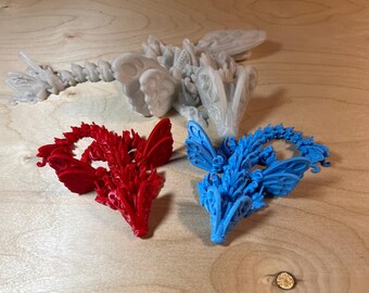 May include: Three 3D printed dragon figurines. One is white, one is red, and one is blue. Each dragon has intricate details and wings.