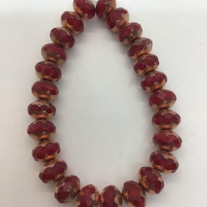 Può includere: Una collana di perline di vetro rosso e rame con finitura sfaccettata. Le perline sono infilate su un filo trasparente.