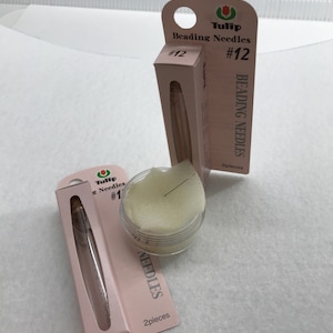 May include: Two packages of Tulip beading needles, one package is size #12 and the other is size #1. Both packages are pink and white with the Tulip logo. The packages are sitting on a white surface.