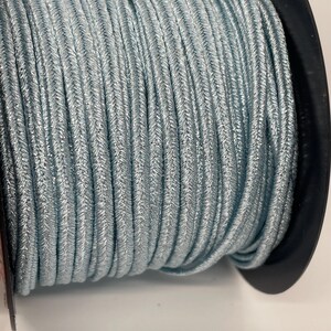 May include: A spool of light blue elastic cord with a silver shimmer. The cord is wound tightly around a black spool.