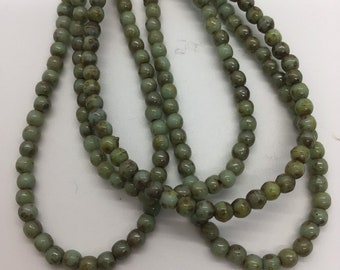 Könnte beinhalten: Eine Strähne grüner Glasperlen mit gesprenkeltem Finish. Die Perlen sind rund und haben eine leicht unregelmäßige Form.