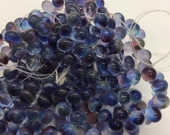 May include: A strand of iridescent blue glass beads, each bead is slightly different in shape and color, creating a unique and beautiful effect.