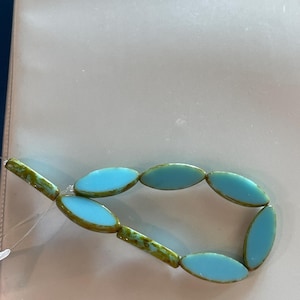 Op de afbeelding: Een streng ovale turquoise blauwe glazen kralen met een groen en bruin marmerpatroon.