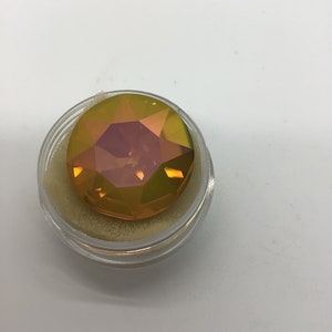 Peut inclure: Une pierre précieuse ronde et irisée avec un design multi-facettes. La pierre précieuse est un mélange de teintes jaunes, orange et roses. Elle est présentée dans un récipient en plastique transparent avec une doublure en mousse blanche.