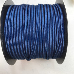 May include: A spool of dark blue elastic cord. The cord is wound tightly around a black plastic spool.