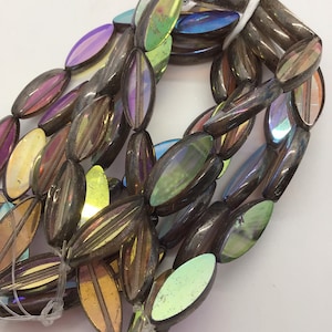 Op de afbeelding: Een streng iriserende glazen kralen in een traanvorm. De kralen zijn donkergrijs met een regenboogkleurige glans.