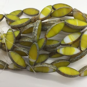 Op de afbeelding: Een streng gele en witte ovale glazen kralen met een gespikkelde bruine afwerking.