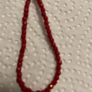 May include: A red beaded necklace with a shiny finish. The beads are small and round, and the necklace is about 18 inches long.