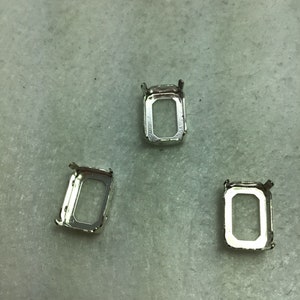 May include: Three silver-toned metal settings for bezel settings. Each setting is rectangular with a smooth, polished finish.