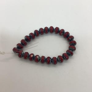 May include: A strand of red and blue faceted beads. The beads are strung together on a thin, clear string, forming a circular shape. The beads have a glossy finish and a speckled pattern.