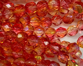 May include: Close-up of a collection of faceted beads in shades of red, orange, and gold. The beads have a sparkling, iridescent finish and are strung together, suggesting they are for jewelry making or crafting.