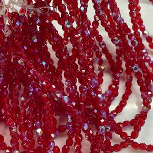 May include: Strands of faceted red beads with iridescent highlights. The beads are strung together, creating a cascading effect. The beads are small and appear to be made of glass or crystal, reflecting light.