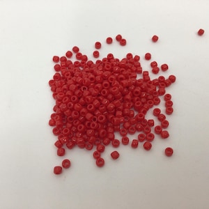 May include: A large pile of small, red, round beads. The beads are scattered on a white surface.