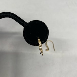 May include: A pair of gold hoop earrings with small clear stones set in the metal. The earrings are on a black velvet display stand.