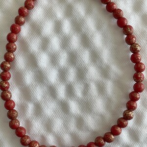 May include: A red beaded necklace with gold flecks. The beads are round and have a slightly textured surface.