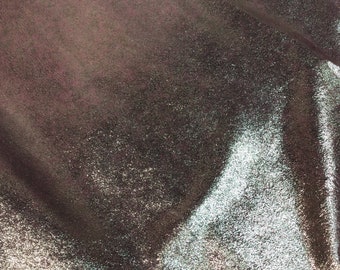 May include: A close-up of a metallic fabric with a shimmery, iridescent finish. The fabric has a textured surface and appears to be a light purple color with silver and gold highlights.